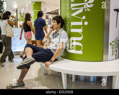 24 août 2013 - Bangkok, Thaïlande - un homme parle sur son téléphone cellulaire dans un centre commercial à Bangkok. La Thaïlande est entré dans une technicalÃ Ã¢ ? ?¢ ?Â récession ce mois après que l'économie s'est contractée de 0,3  % au deuxième trimestre de l'année. La contraction de 0,3  % du produit intérieur brut entre avril et juin, suivie d'une chute de 1,7  % au cours du premier trimestre de 2013. La contraction est imputée à une baisse de la demande pour les exportations, une baisse de la demande intérieure et une perte de confiance des consommateurs. En même temps, la valeur du baht thaïlandais par rapport au dollar américain a chuté considérablement, passant de abou Banque D'Images