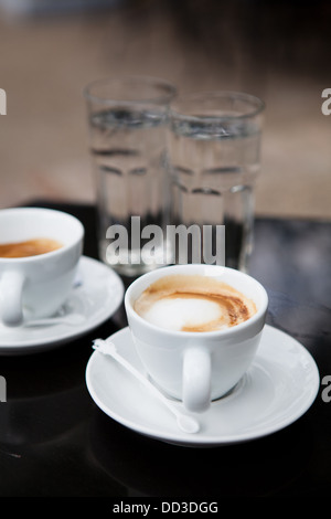 Deux cafés à base de lait en blanc tasses et verres d'eau sur cafe table Banque D'Images