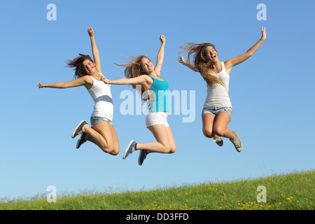 Groupe de trois adolescentes de sauter sur l'herbe avec le ciel bleu en arrière-plan Banque D'Images