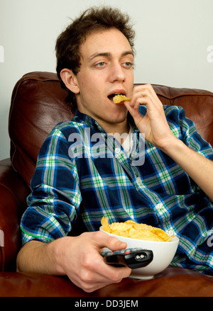 Jeune homme sur couch eating potato chips Banque D'Images