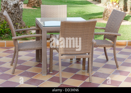 Meubles de patio en plein air de canne avec table en verre et chaises sur le carrelage Banque D'Images