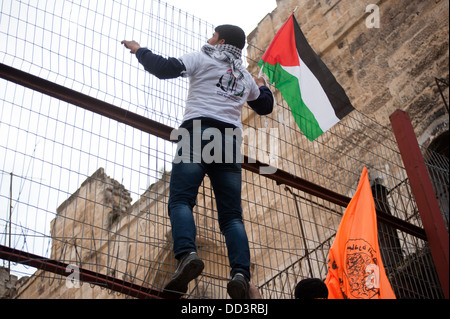 Des manifestants palestiniens escalader une barrière d'acier et de béton rue pendant une manifestation contre l'occupation israélienne à Hébron. Banque D'Images