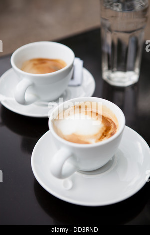 Libre de deux cafés en blanc à base de lait sur les tasses cafe table avec verre d'eau en arrière-plan Banque D'Images