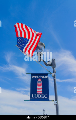 Une bienvenue à Lubec sign est suspendu une lampe de rue avec un drapeau américain qui flotte dans la brise. Banque D'Images