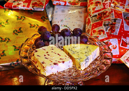 Wensleydale avec canneberges et fromage stilton bleu avec raisins rouges sur une plaque de verre avec des cadeaux de Noël à l'arrière Banque D'Images