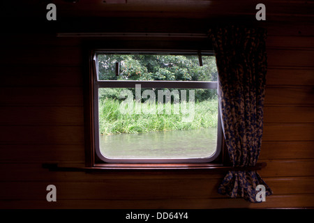 La vue à la recherche d'une fenêtre sur un petit bateau qui flotte sur la rivière Kennet and Avon, Berkshire, Angleterre. Banque D'Images