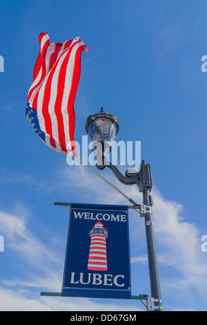 Une bienvenue à Lubec sign est suspendu une lampe de rue avec un drapeau américain qui flotte dans la brise. Banque D'Images