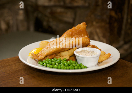 Fish, chips, petits pois et sauce tartare sur une assiette blanche dans un pub Banque D'Images