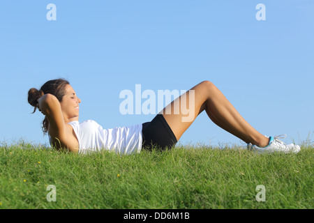 Vue latérale d'une belle femme faisant des craquements dans l'herbe avec le ciel en arrière-plan Banque D'Images