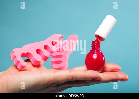 Accessoires pédicure vernis à ongles rouge et rose sur les séparateurs d'orteil main femme fond bleu Banque D'Images