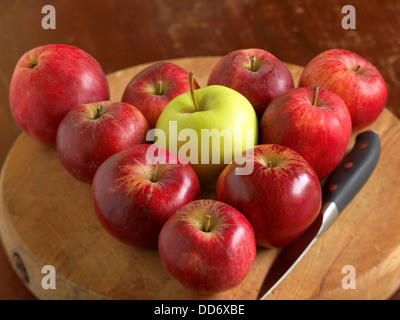 Un tas de pommes rouges disposées en triangle avec la pomme verte au milieu et un couteau sur la planche à découper. Banque D'Images