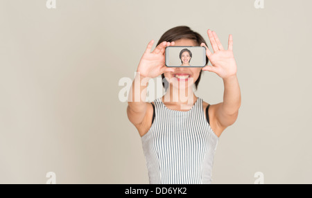 Jeune femme sourire et prendre une photo d'elle-même avec l'appareil photo dans un téléphone mobile Banque D'Images