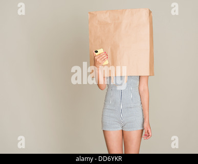 Anonyme. Jeune femme avec sac de papier sur la tête tenant un téléphone mobile. Banque D'Images