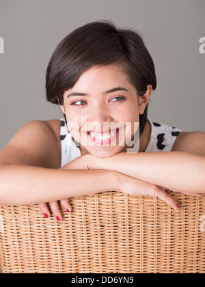 Young woman sitting in wicker chair looking away and smiling Banque D'Images