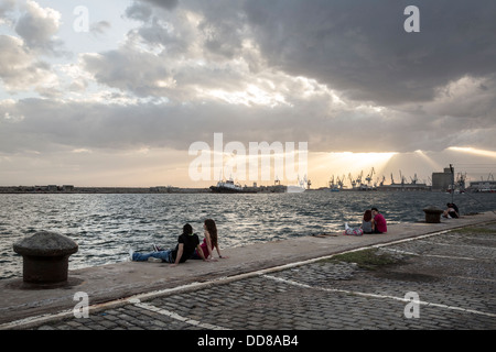 Les jeunes couples assis au bord du port de Thessalonique pendant le coucher du soleil. Banque D'Images