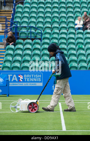 Groundsman peint les lignes blanches sur un court de tennis avec une machine en tant que spectateurs watch sur les stands Banque D'Images