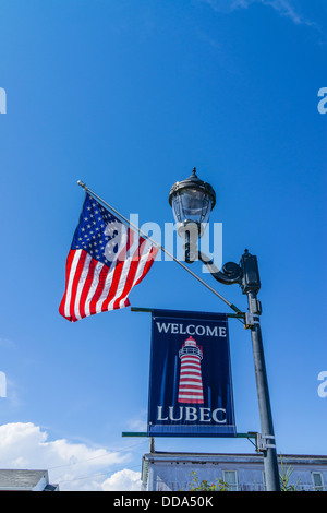 Une bienvenue à Lubec sign est suspendu une lampe de rue avec un drapeau américain qui flotte dans la brise. Banque D'Images