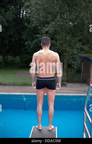 Homme debout sur le plongeoir à piscine public prêt à sauter Banque D'Images