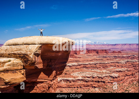 Homme avec les bras tendus se tient sur une falaise dans la région de Island in the Sky District Canyonlands National Park, en Utah. Crack blanc blanc le long de la route de Rim. Banque D'Images