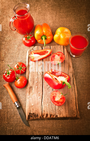 Jus de légumes biologiques frais, les tomates, le paprika, l'acier couteau et planche à découper en bois sur toile cirée. Style Vintage Banque D'Images