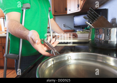 Après l'homme ligament croisé antérieur (LCA) avec des béquilles la cuisson dans la cuisine Banque D'Images