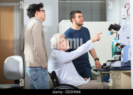 Le professeur ayant la dystrophie musculaire en travaillant avec des étudiants ingénieurs à la recherche de x-ray fluorescence analyzer dans un laboratoire Banque D'Images