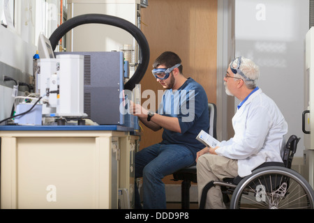 Le professeur avec la dystrophie musculaire et une étudiante en génie à l'aide de l'analyseur thermogravimétrique dans un laboratoire Banque D'Images