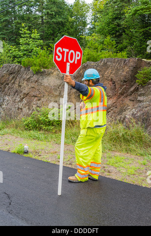 Le signaleur, habillé dans des vêtements de couleur jaune-vert est titulaire d'un signe de la circulation pour arrêter les voitures en cours d'un projet de construction de route. Banque D'Images