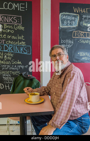 Un homme aux cheveux gris est assis à une table de restaurant manger sa soupe pour le déjeuner et fait face à l'avant avec cuillère dans sa main. Banque D'Images