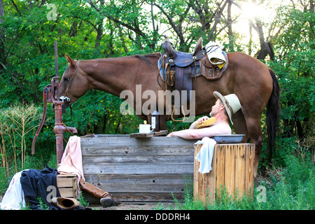 Un cowboy echelle et rasage le matin avec son cheval Banque D'Images