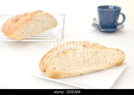 Des tranches de pain focaccia au romarin et l'ail sur une plaque, avec le pain coupé sur une grille de refroidissement à l'arrière-plan Banque D'Images