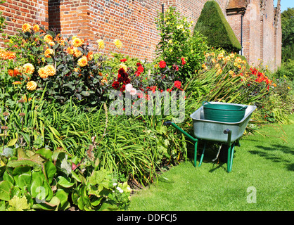 Brouette garée à côté d'une frontière colorée de fleurs d'été dans un jardin clos Banque D'Images