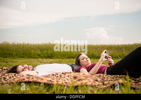 Jeune couple relaxant à l'extérieur dans la nature - femme avec le smartphone se trouve sur l'homme Banque D'Images