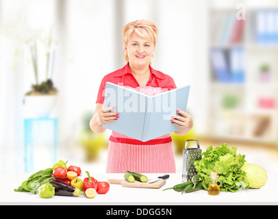 Smiling mature femme cuisinière avec tablier et cookbook preparing salad Banque D'Images