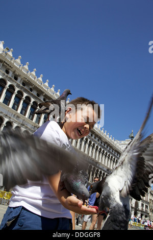 Boy feeding pigeons en plein air sur la place San Marco, Venise Italie