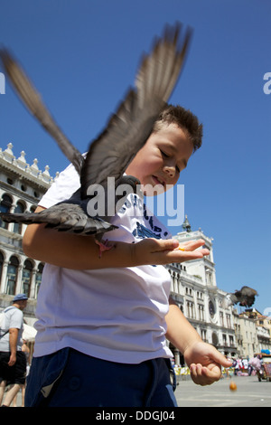 Boy feeding pigeons en plein air sur la place San Marco, Venise Italie