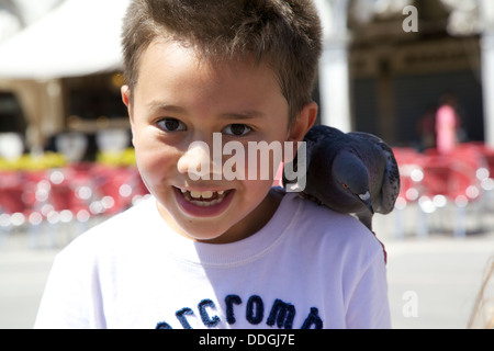 Boy feeding pigeons en plein air sur la place San Marco, Venise Italie