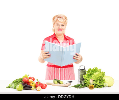 Smiling mature femme cuisinière avec tablier et livre de recettes preparing salad Banque D'Images