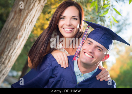 Heureux homme diplômé en Cap and Gown et jolie fille célébrer à l'extérieur. Banque D'Images