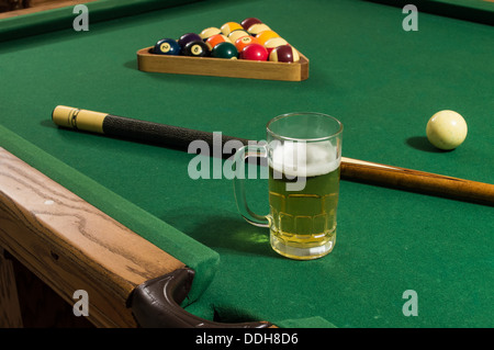 Une bière froide avec de la mousse sur une table de billard avec feutre vert, un pool stick et rack de 15 boules dont 8 balle et 9 balle. Banque D'Images