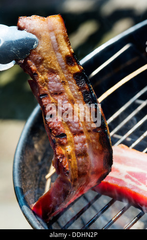 Deux gros morceaux de bacon le grill.On est pris avec des pinces Banque D'Images