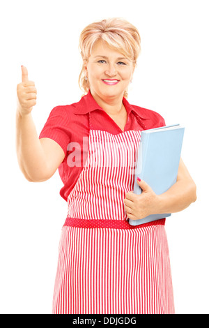 Smiling mature femme cuisinière avec un livre de cuisine et tablier holding giving thumb up Banque D'Images