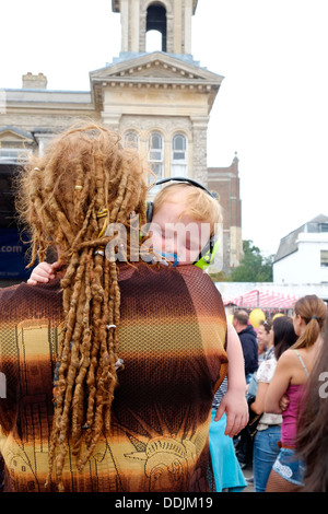 Un jeune garçon, bercée dans les bras de son père dreadlocked, prend une sieste rapide portant son protège-oreilles Carnaval 2013 à Kingston. Banque D'Images