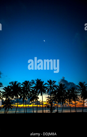 Les îles Cook, l'île d'Aitutaki, coucher du soleil tropical couleurs avec silhouette de palmiers et un croissant de lune se lève au-dessus de Ouargla Beach Banque D'Images