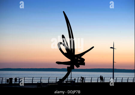 Port Talbot - South Wales - UK - 3 septembre 2013 : les gens marcher au-delà de la sculpture Trail' 'Kite au coucher du soleil le long du front de mer à Aberavon Beach près de Port Talbot, ce soir. Le Cerf-volant Trail sculpture à Aberavon est Wales' plus grande sculpture debout à 12 mètres de haut et pesant 11 tonnes. Il a été conçu par l'artiste réalise et sculpteur Andrew Rowe et a été installé en décembre 2007. © Phil Rees/Alamy Live News Banque D'Images