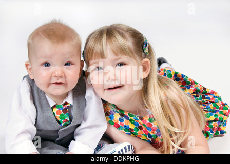 Petite fille couchée sur son ventre s'étire jusqu'à son petit frère, habillé en costume et cravate et l'appariement spotty dress, UK Banque D'Images