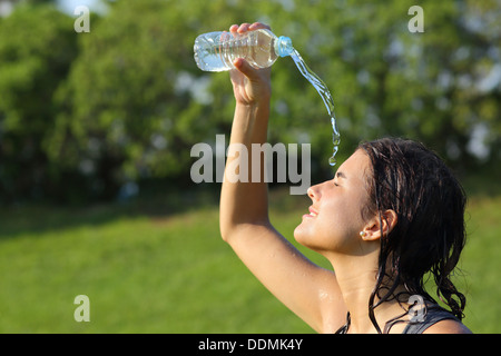 Belle femme se jetant de l'eau d'une bouteille avec un fond vert Banque D'Images