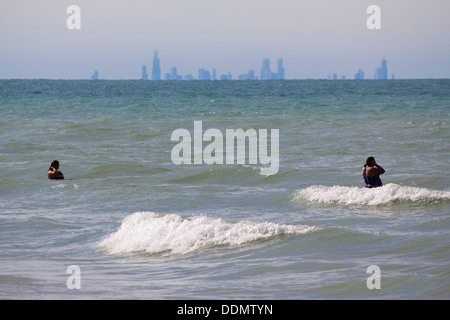 Les baigneurs pataugent dans le surf à l'Indiana Dunes State Park avec le centre-ville de Chicago sur l'horizon lointain, la courbure de la terre inférieure obscurcissant les bâtiments. Banque D'Images