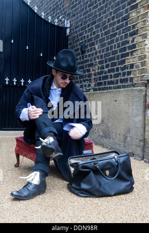 Homme portant un étrange manteau noir et un chapeau assis sur banquette sur le sable près de valise dans la pluie et la neige Banque D'Images