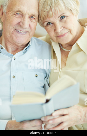 Portrait d'un franc senior couple looking at camera while reading book together Banque D'Images